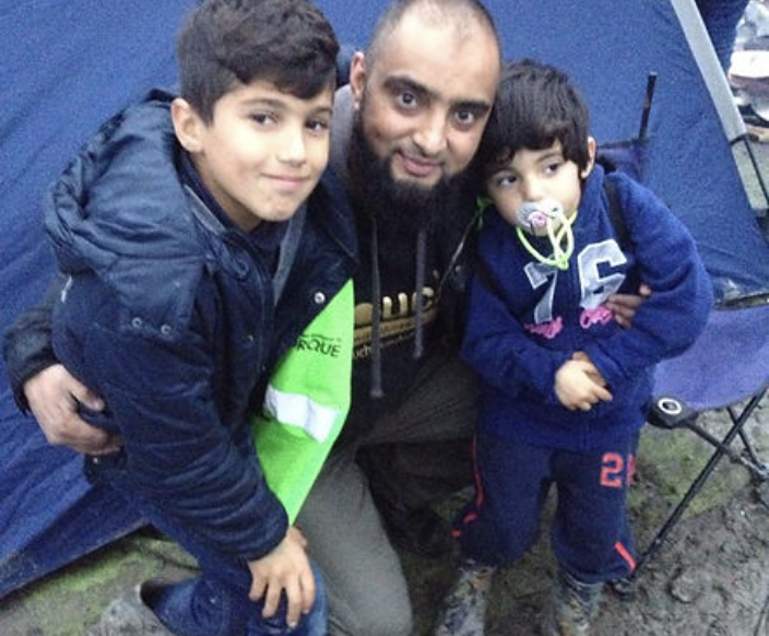 A man posing with his arms around two young boys.